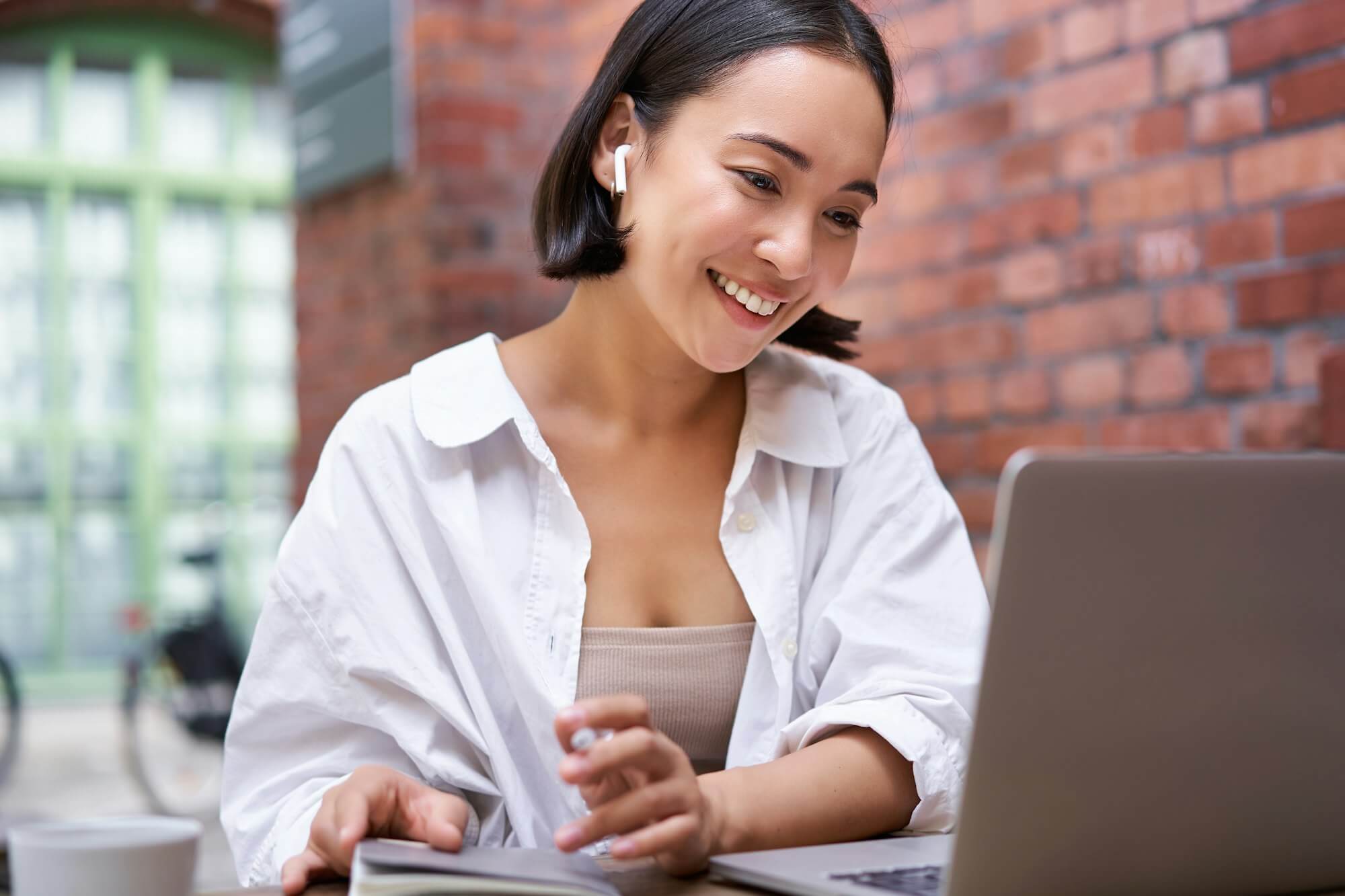 young-smiling-asian-woman-with-wireless-earphones-sitting-in-coworking-office-space-with-laptop.jpg